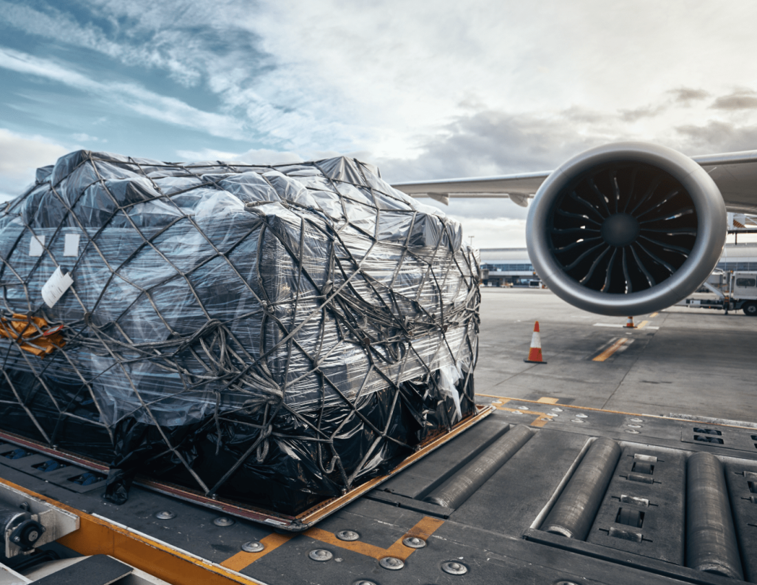Packaged air cargo secured with ropes, sitting next to airplane wing on a runway