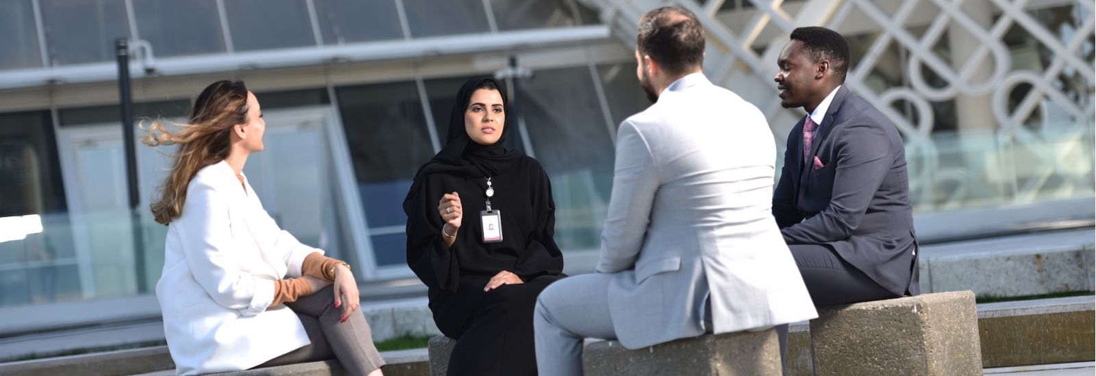 Group of four people men and women of multiple ethnicities, sitting in a circle outside of an office, having a discussion