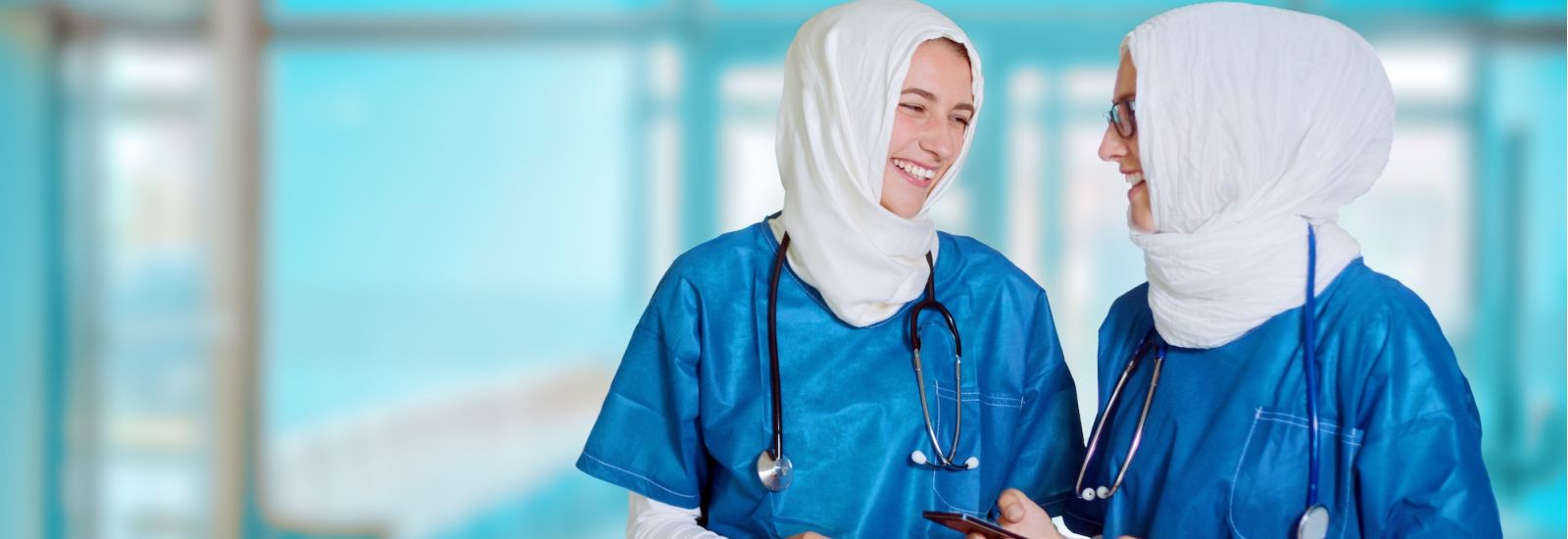 Two happy female middle eastern doctors in blue medical uniform standing in a hospital hallway