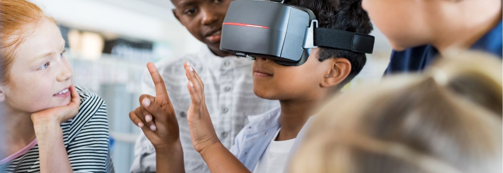 Mixed race child with vr virtual reality goggles in classroom with his friends.