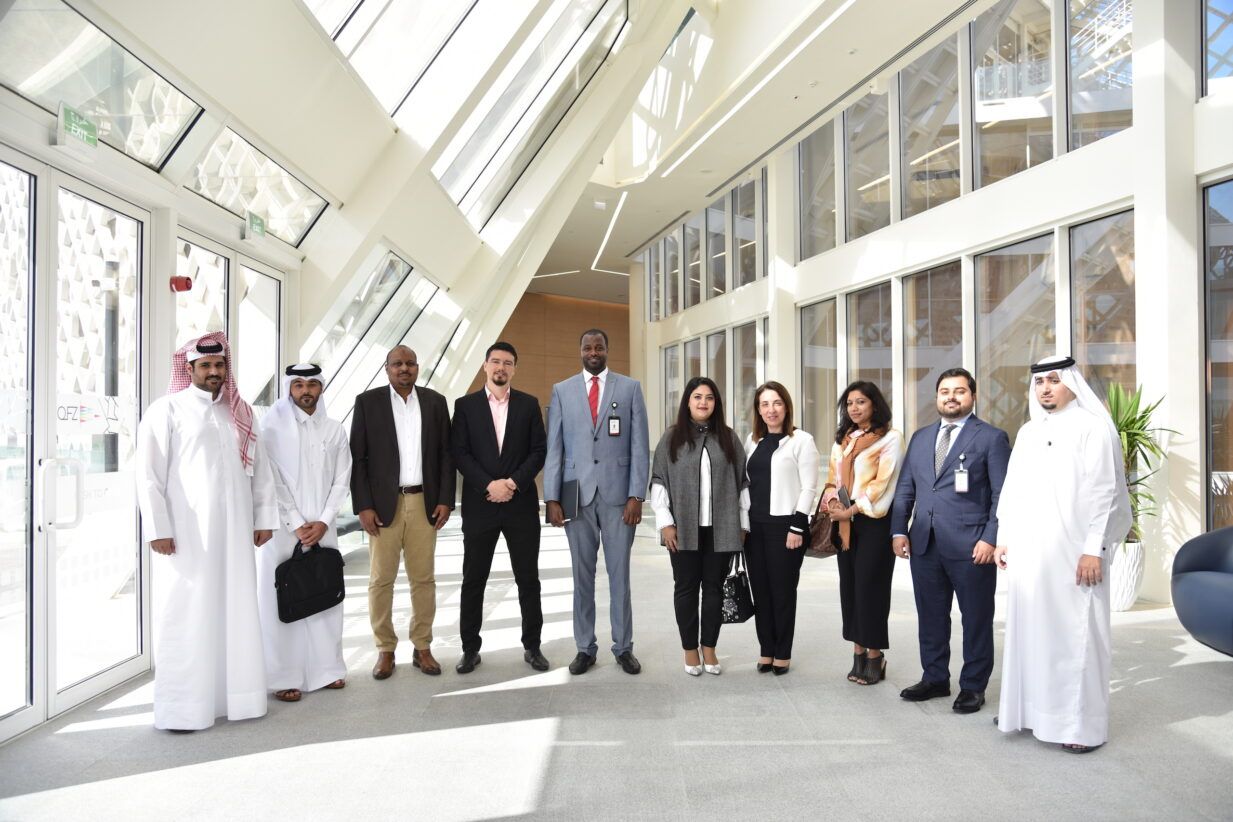 Qatar Free Zones Authority's diverse investor support team, standing in line smiling at a camera
