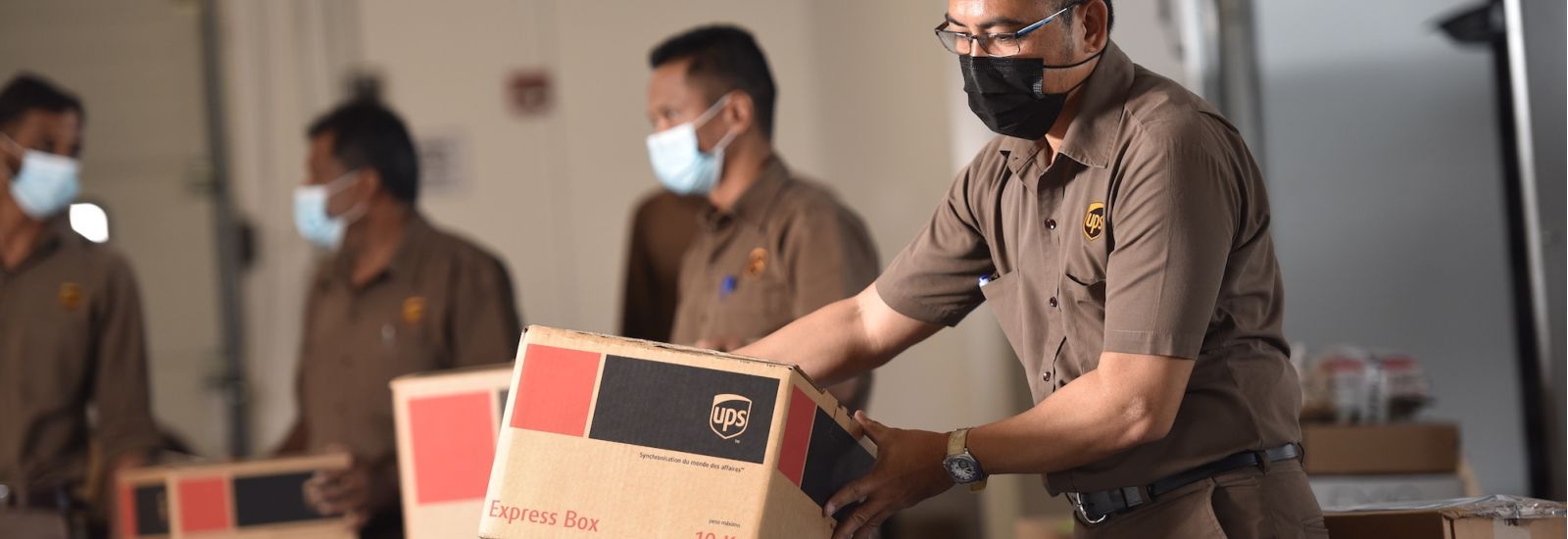UPS packaging facility, workers in brown uniforms with masks handling packages