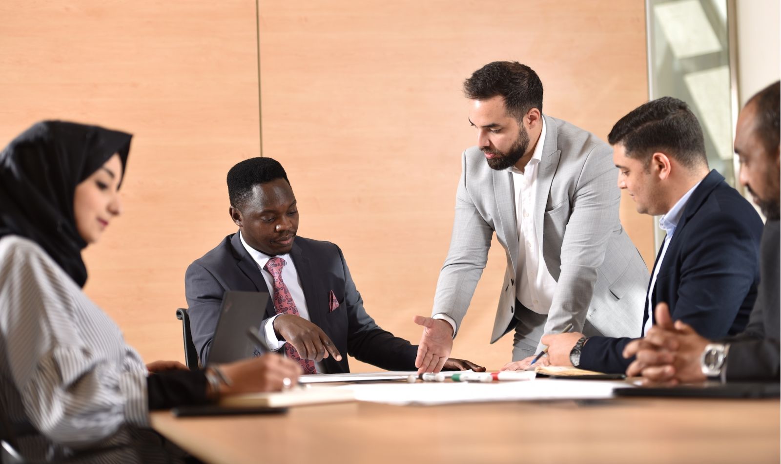 Diverse group sitting in a conference room, having a discussion while pointing at papers