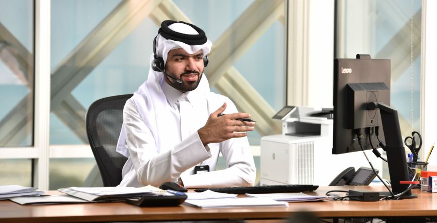 Man in traditional Arabic clothing, sitting at a desk with a headset on, taking a call