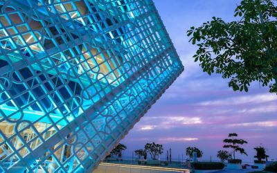 Exterior view of the Business Innovation Park in Ras Bufontas Free Zone, featuring illuminated geometric facade architecture overlooking the Doha waterfront at sunset.
