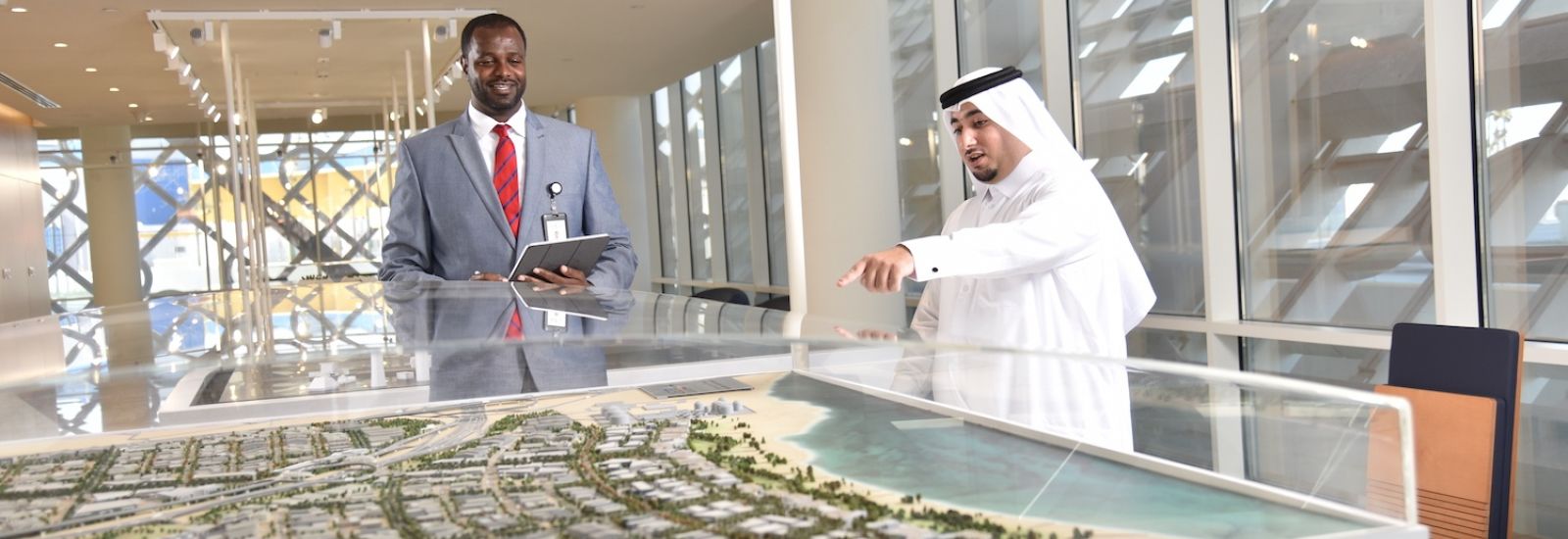 Two men, one in a suit and one in traditional Arabic clothing, pointing at a 3-D map of the Qatar Free Zones